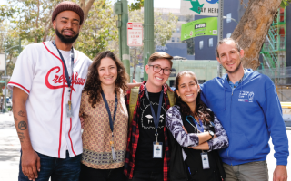 a photo with 5 people of different ages, races, and genders standing together closely